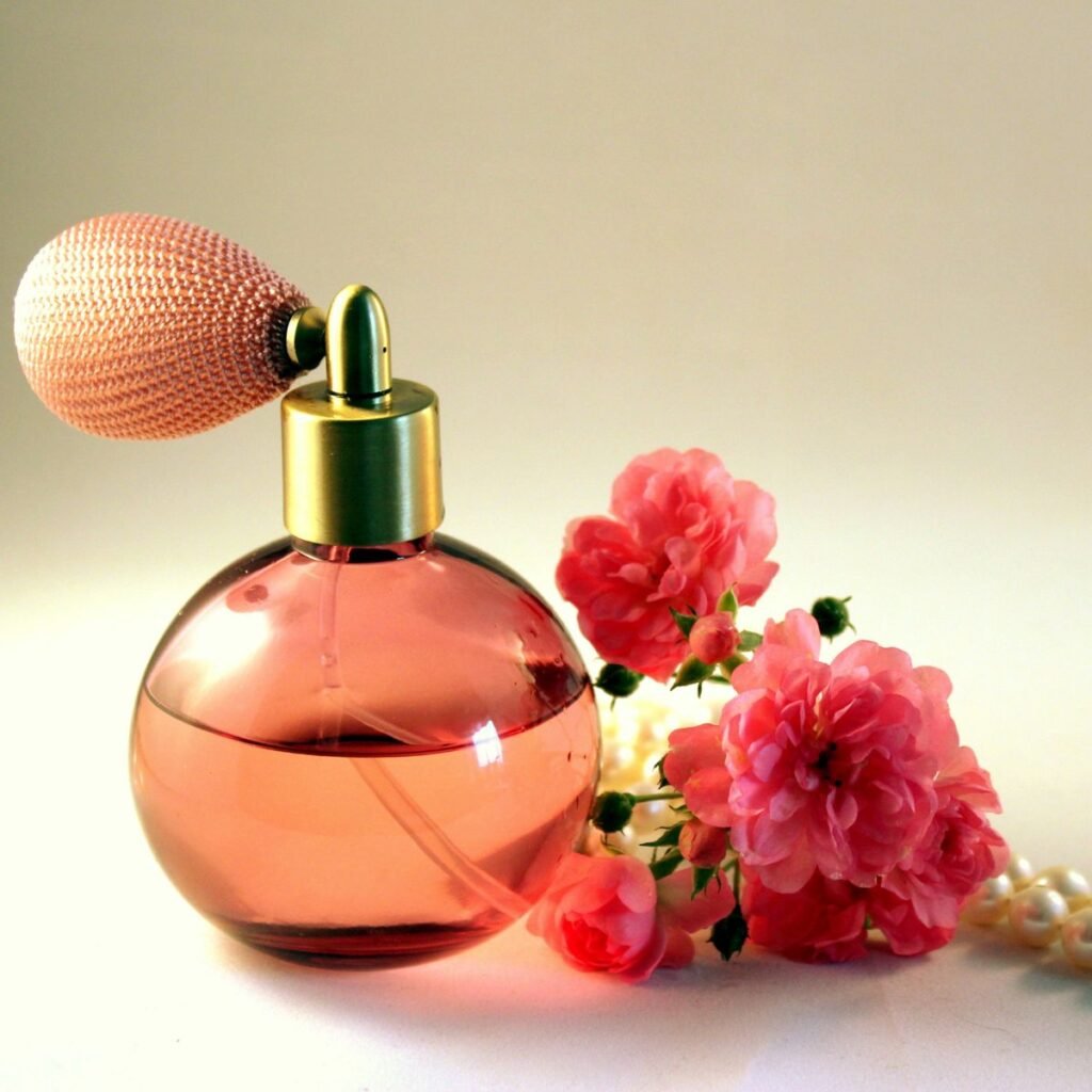 A psicologia por tras dos perfumes, como os perfumes influenciam e demonstram nossa personalidade. A imagem mostra um perfume em um frasco avermelhado com flores ao redor.