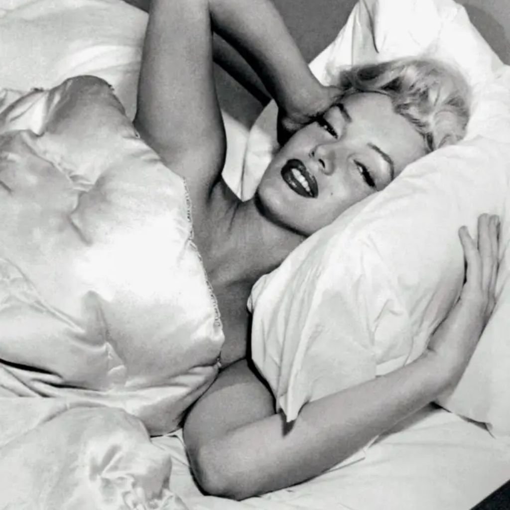 Fotografia da atriz Marilyn Monroe deitada entre os lençõis.